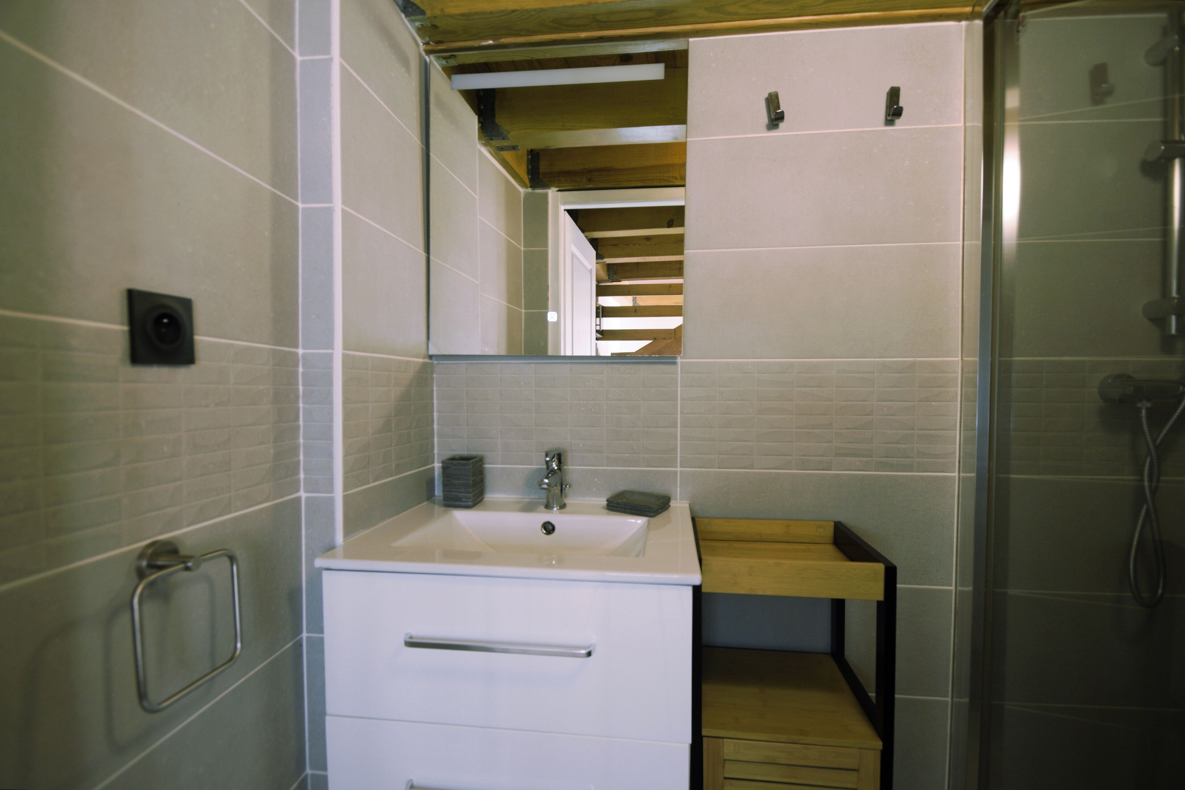 A modern bathroom with a white sink, mirror, and wooden shelf.