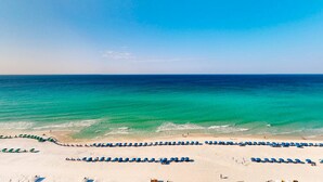 Une plage bordée de rangées de parasols bleus et de chaises longues, un rivage sablonneux et l’océan.