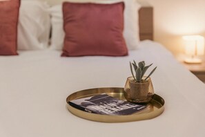 Ein ordentlich bezogenes Bett mit einer Zeitschrift auf einem Tablett, einer kleinen Topfpflanze und einer Lampe auf dem Nachttisch.