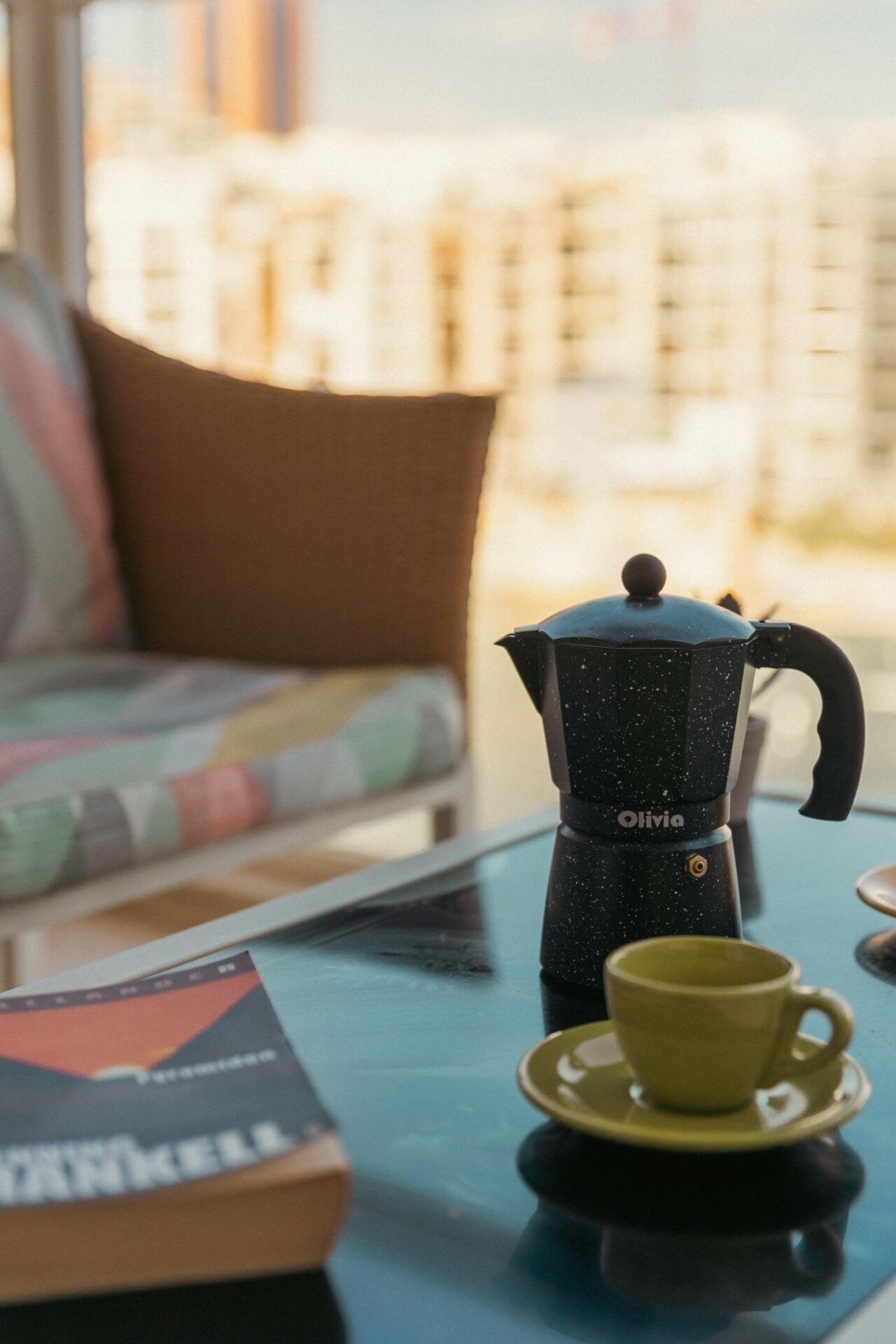 Une table sur laquelle on a disposé une cafetière noire, une tasse jaune et un livre.