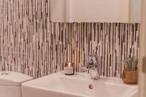 Ein Badezimmer mit einem weißen Waschbecken, einem Spiegel darüber und einer strukturierten Wand im Hintergrund.