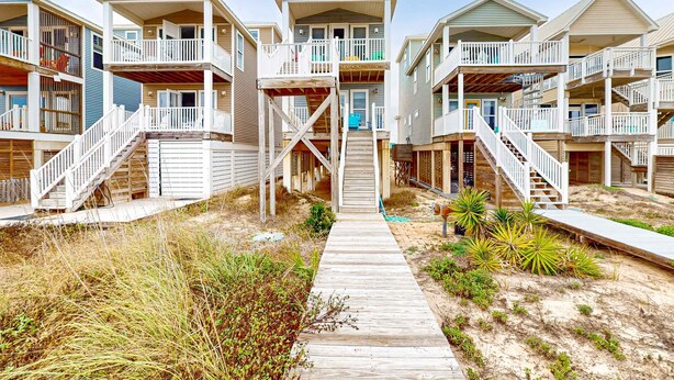 Un hotel frente a la playa con edificios de varios pisos, pasarelas de madera y escaleras exteriores.
