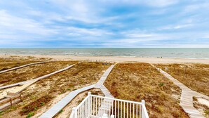 Una playa con un paseo marítimo de madera que conduce al agua, dunas de arena y un cielo despejado.