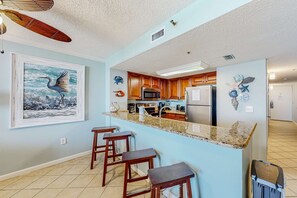 Una cocina con armarios de madera, encimera de granito y microondas. Hay tres taburetes de madera y un cuadro con la imagen de un pájaro en la pared.