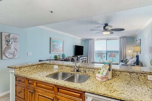 A kitchen with granite countertops, a double sink, wooden cabinets, and a ceiling fan. - Beachfront Escape with Gulf Views, Pool & Hot Tub (Destin)