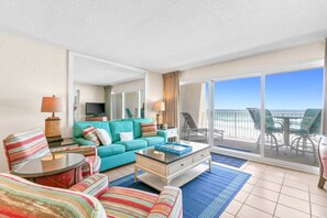Ein Hotelzimmer mit Balkon, einem petrolfarbenen Sofa, gestreiften Sesseln, einem Couchtisch und einem Fernseher.
