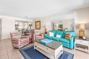 Un salon avec des fauteuils à rayures, un canapé de couleur turquoise et une table basse en verre.