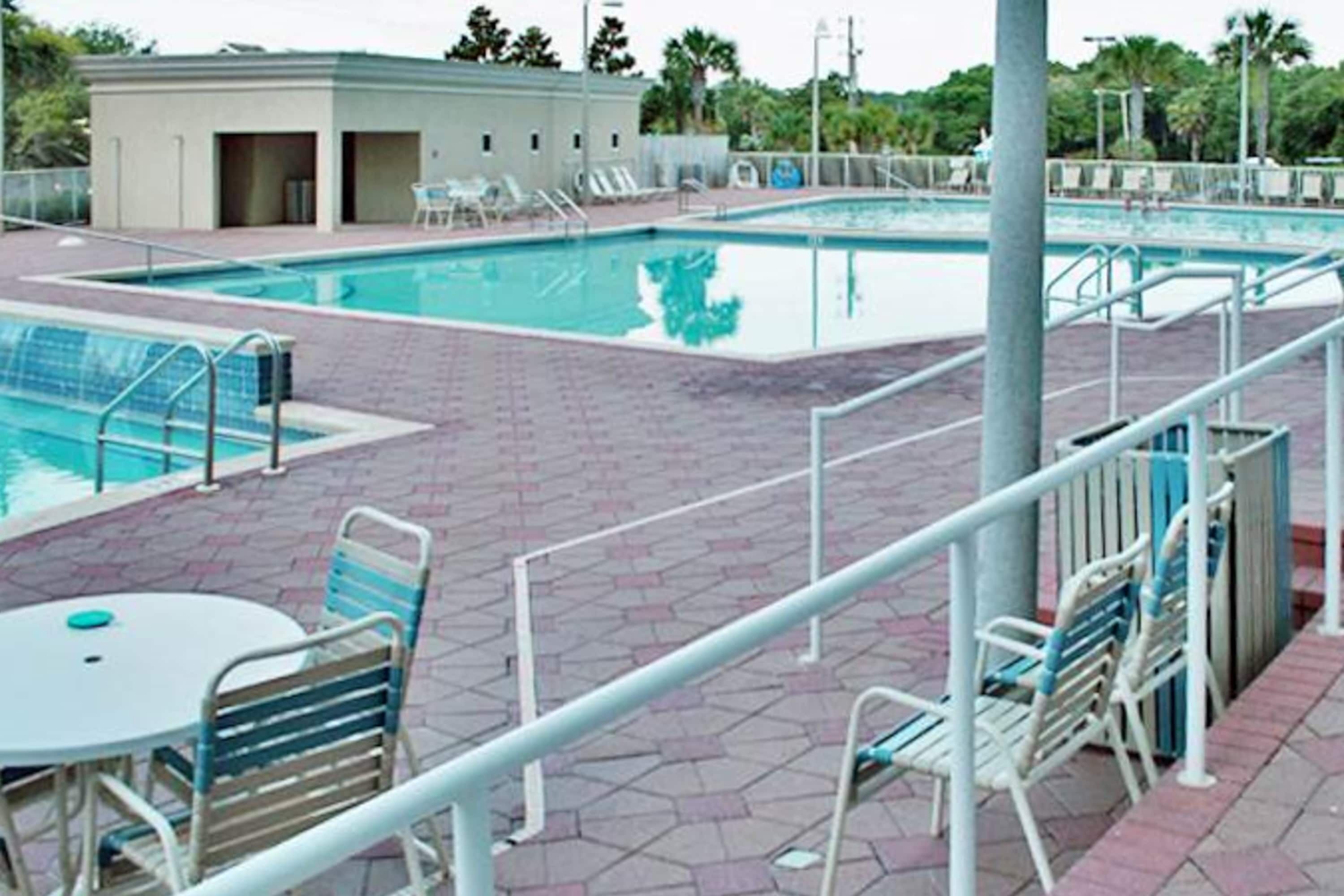 A swimming pool with a tiled deck, lounge chairs, and a small building in the background.