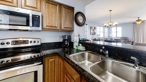 A modern kitchen with stainless steel appliances, wooden cabinets, a large sink, and a dining area in the background. - Spacious 3 Bedroom Condo with Beach Views and Resort Pool Access (Miramar Beach)