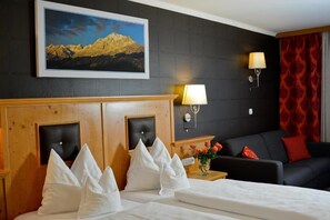A hotel room with a bed, a sofa, a painting of mountains, and a lamp. - Hotel Rettenberg (Kolsass)