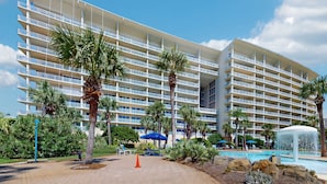 Ein mehrstöckiges Hotel mit Balkonen, einem Swimmingpool und Palmen.
