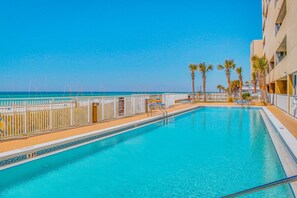 Una piscina con vista al océano, palmeras y un edificio con balcones.