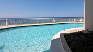 A clear blue pool with a white railing, surrounded by a concrete deck and some flowers. - Oceanfront condo with pool, hot tub & washer/dryer (Panama City Beach)