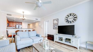A modern living room with a light blue sofa, a wooden coffee table, and a large flat-screen TV. - Oceanfront condo with pool, hot tub & washer/dryer (Panama City Beach)
