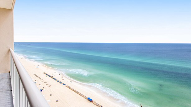 A beach view from a balcony with a clear sky, a sandy beach, and a calm sea. - Oceanfront condo with pool, hot tub & washer/dryer (Panama City Beach)