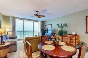 A spacious living room with a dining table, sofas, and a ceiling fan. - Beachfront condo rental with pools, hot tub, and private balcony (Panama City Beach)