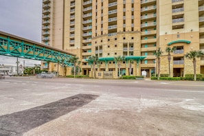 A multi-story hotel with a stone facade, a green pedestrian bridge, and palm trees. - Updated, beachfront condo with pool, hot tub & gym (Panama City Beach)