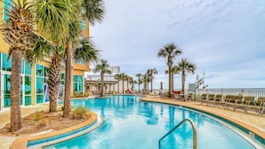 A swimming pool with palm trees, a building with large windows, and a view of the ocean. - Updated, beachfront condo with pool, hot tub & gym (Panama City Beach)