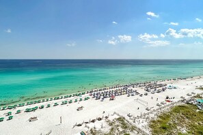 A beach with rows of umbrellas and beach chairs, a sandy shore, and the ocean. - Emerald Towers 0202 (Destin)