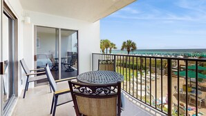 Ein Balkon mit Tisch und Stühlen, mit Blick auf einen Strand mit Sonnenschirmen und Liegestühlen.