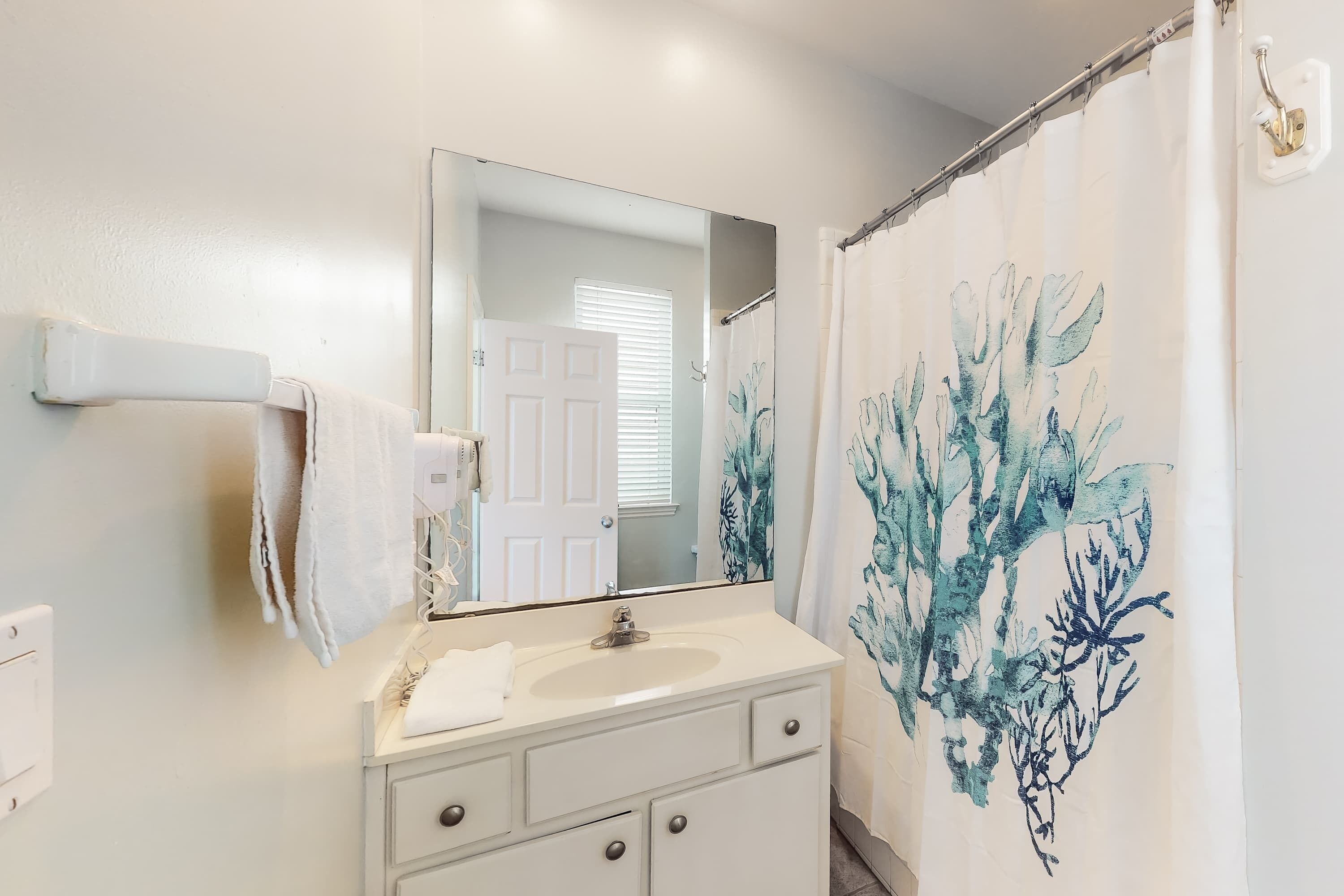 A bathroom with a white sink, a mirror, and a shower curtain with a blue coral design.