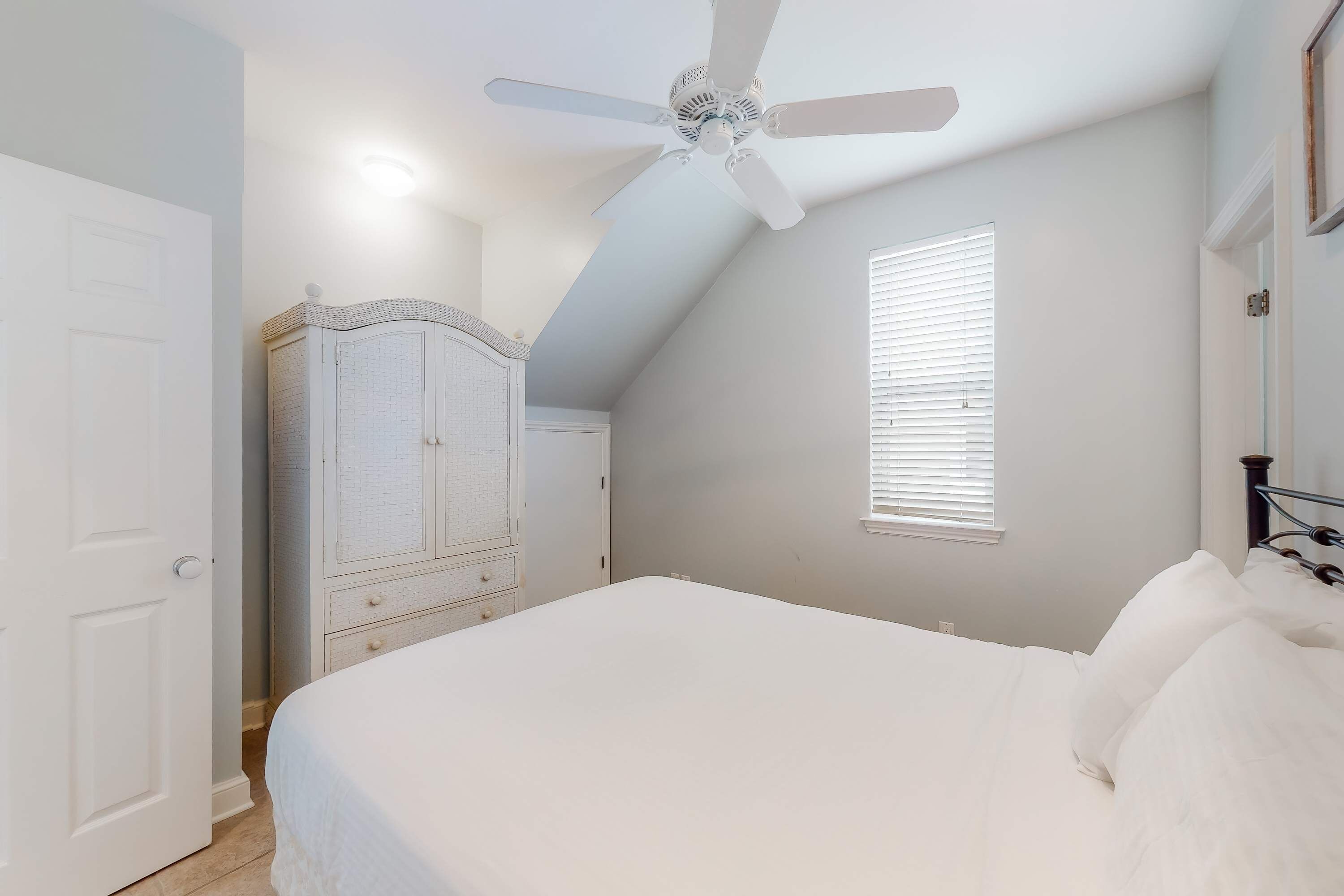 A bedroom with a bed, a ceiling fan, a wardrobe, and a window with blinds.