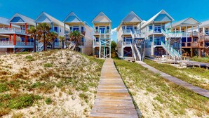 Un hotel frente a la playa con edificios de varios pisos, pasarelas de madera y una zona de arena.
