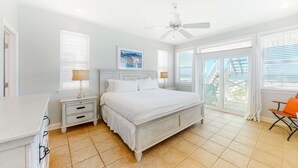 Un dormitorio con cama, mesitas de noche, ventilador de techo y vistas al exterior.