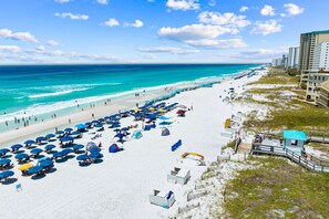 Ein Strand mit vielen Sonnenschirmen und Liegestühlen, einem Rettungsturm und einer Promenade, die zum Strand führt.