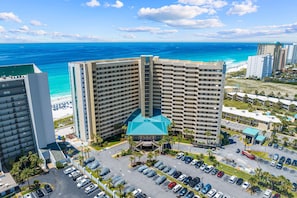 A high-rise hotel with a central atrium, parking lot, and a view of the ocean. - Ocean-view condo at SunDestin with pool, hot tub, sauna, and walkable locale (Destin)