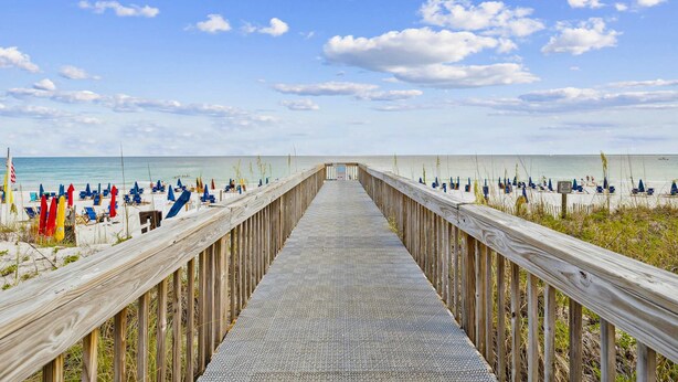 Una passerella in legno che conduce a una spiaggia con ombrelloni e lettini.