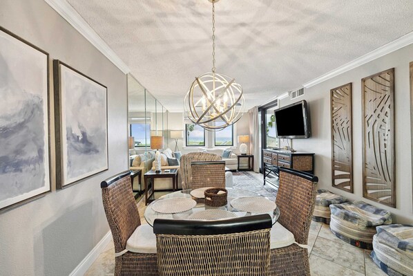 A dining area with a round table, wicker chairs, and a modern chandelier. - Jetty East 117B (Destin)