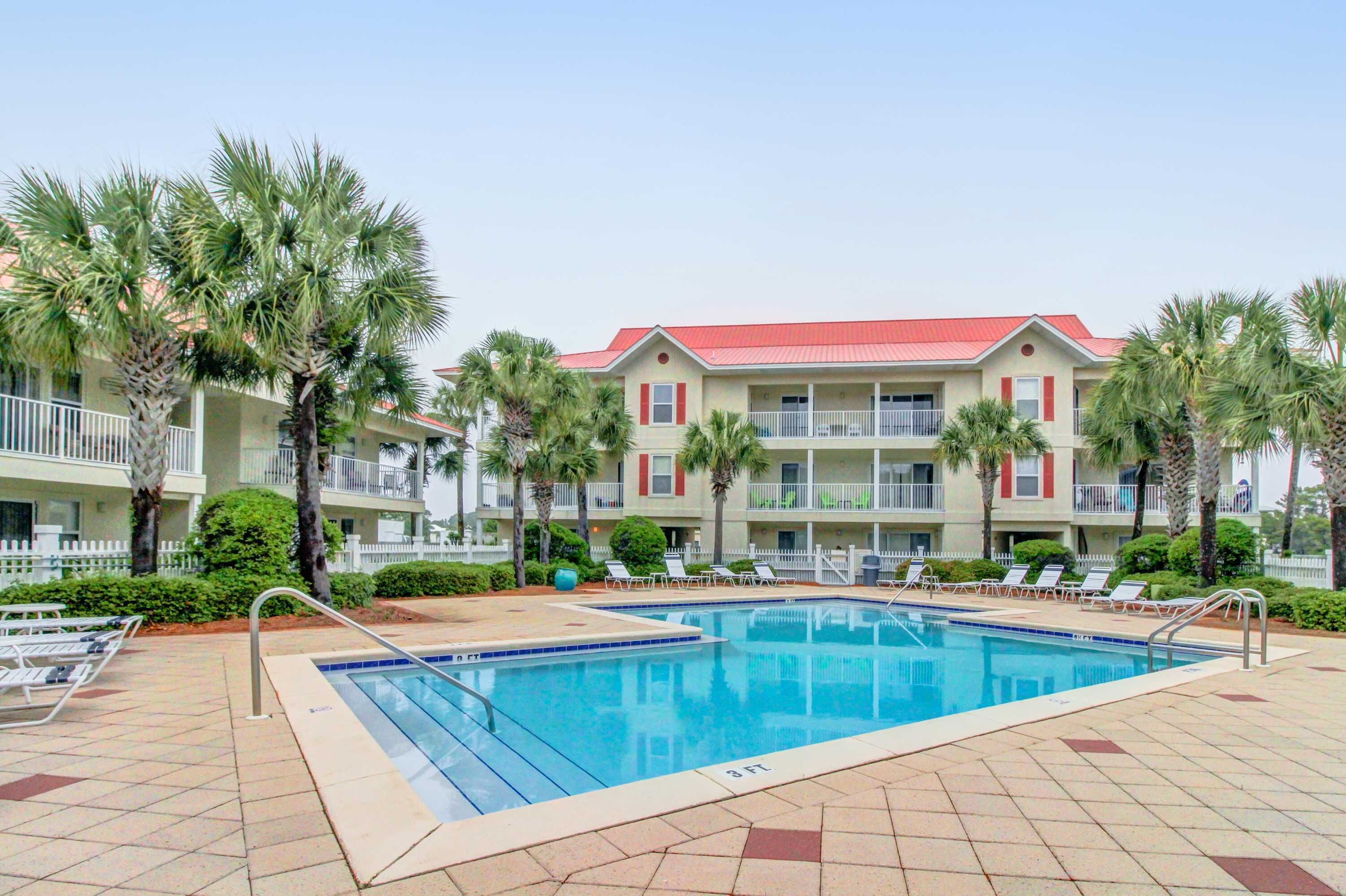 A hotel with a swimming pool, palm trees, and a red-roofed building.