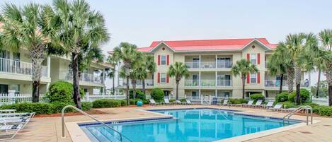A hotel with a swimming pool, palm trees, and a red-roofed building.