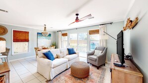 Ein geräumiges Wohnzimmer mit einem weißen Sofa, einem grauen Sessel und einem großen Fernseher auf einem Holzboden.