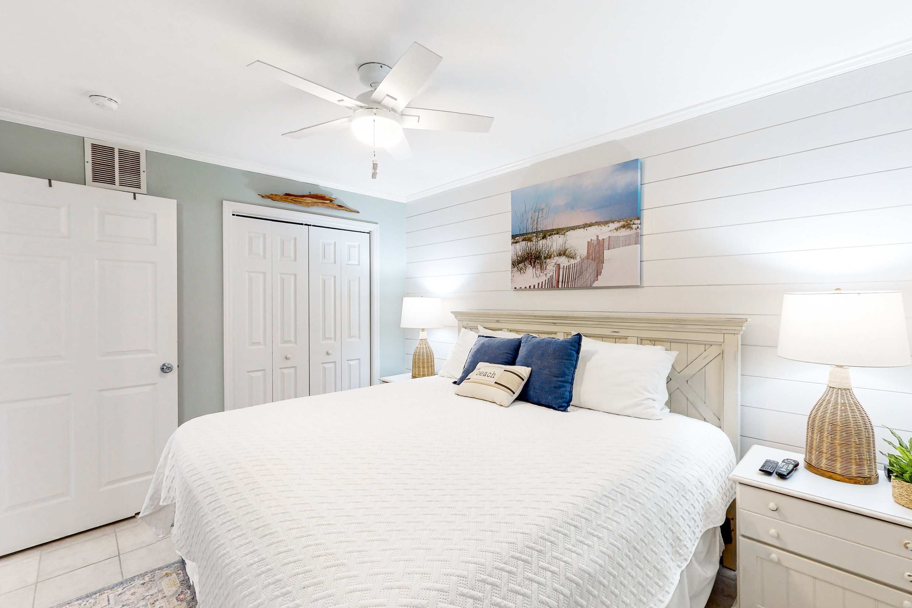 A bedroom with a bed, nightstands, a ceiling fan, and a wall-mounted painting.