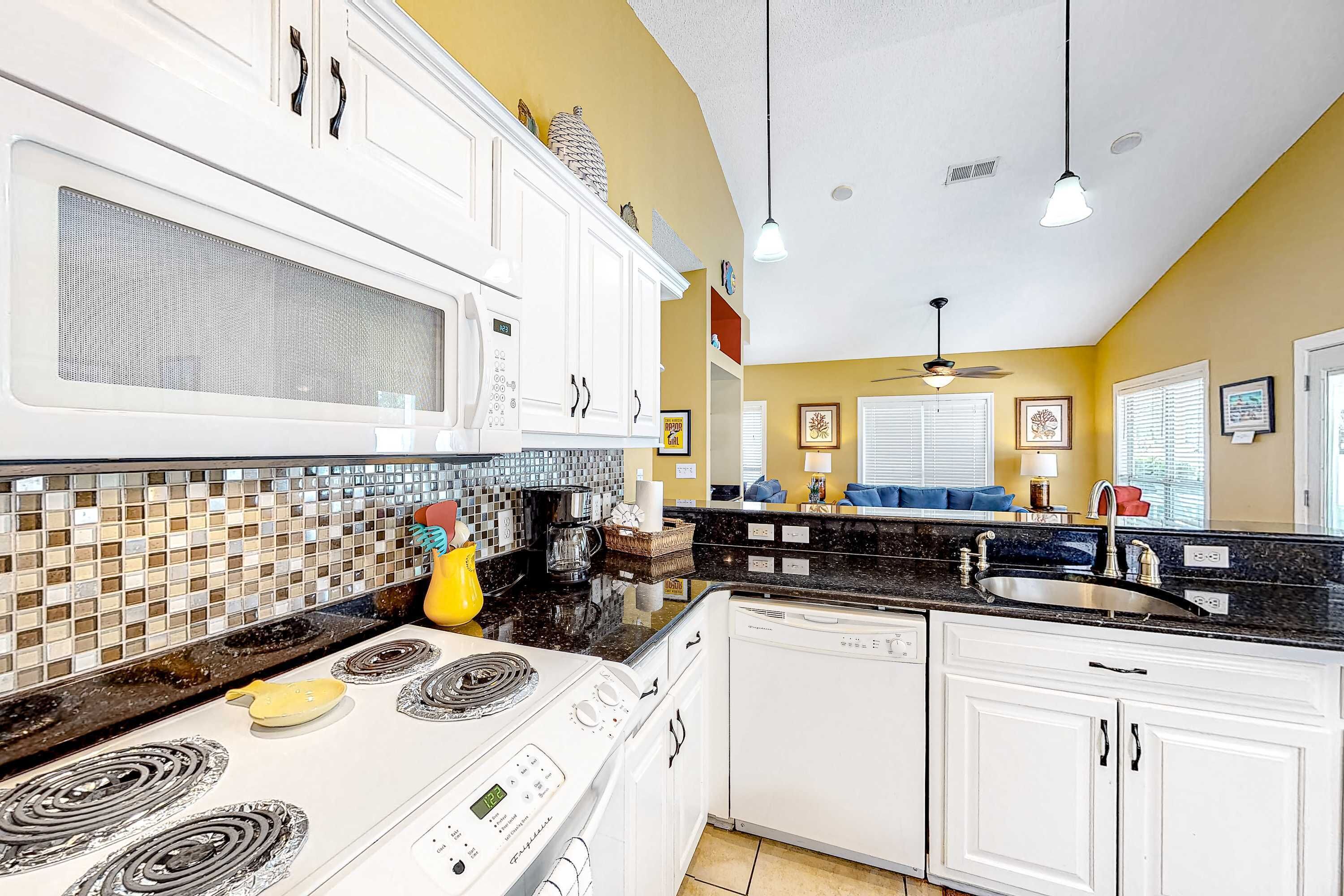 A kitchen with white cabinets, a black countertop, and a stove.