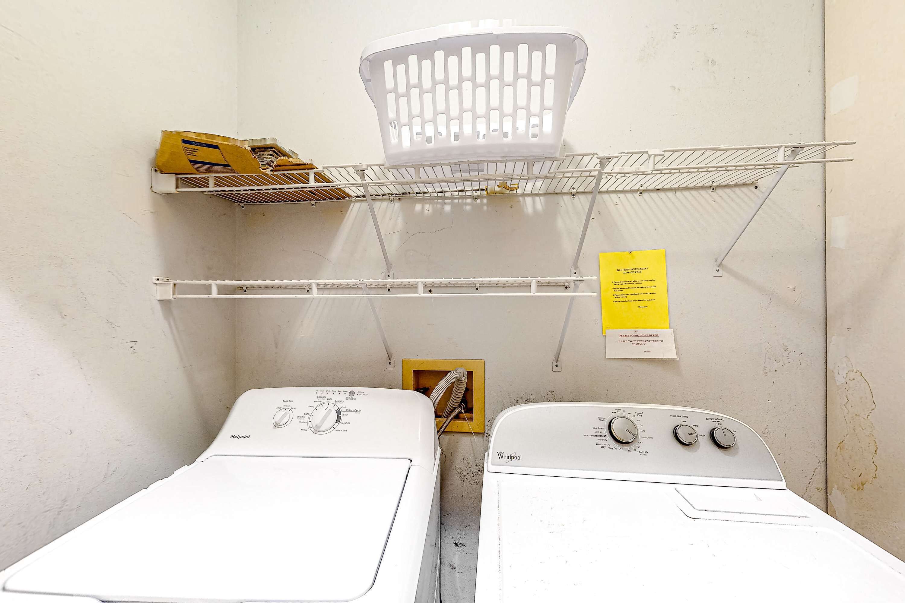 A laundry room with two front-loading washers, a metal shelf, and a yellow sign.