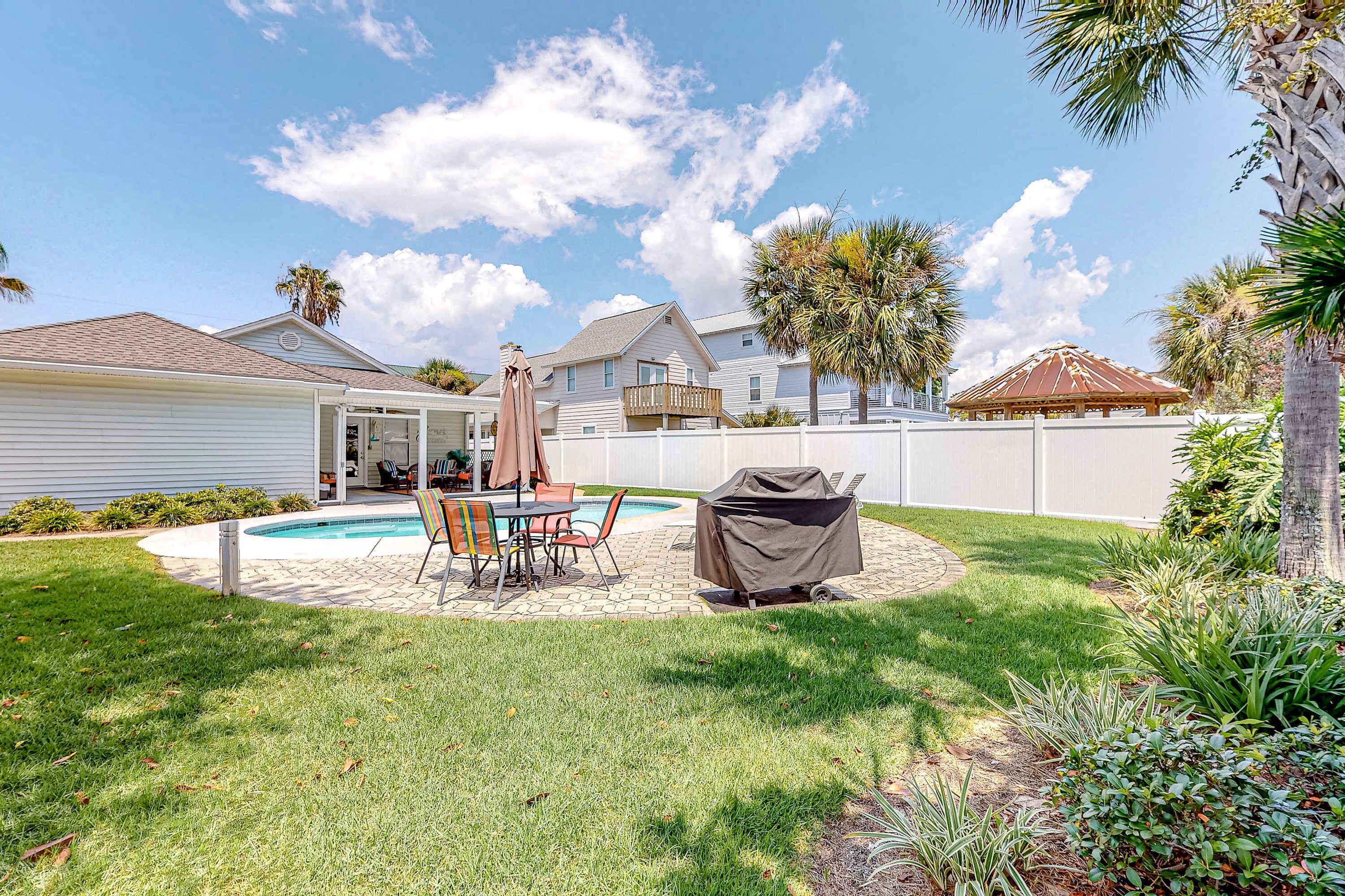 Un jardin avec une piscine, des meubles de patio et un espace barbecue couvert.