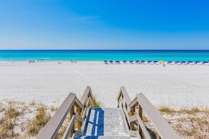 A beach with a wooden staircase leading to the sand, a clear blue sky, and a calm sea. - Destiny West - Cincy in the Sun (Destin)