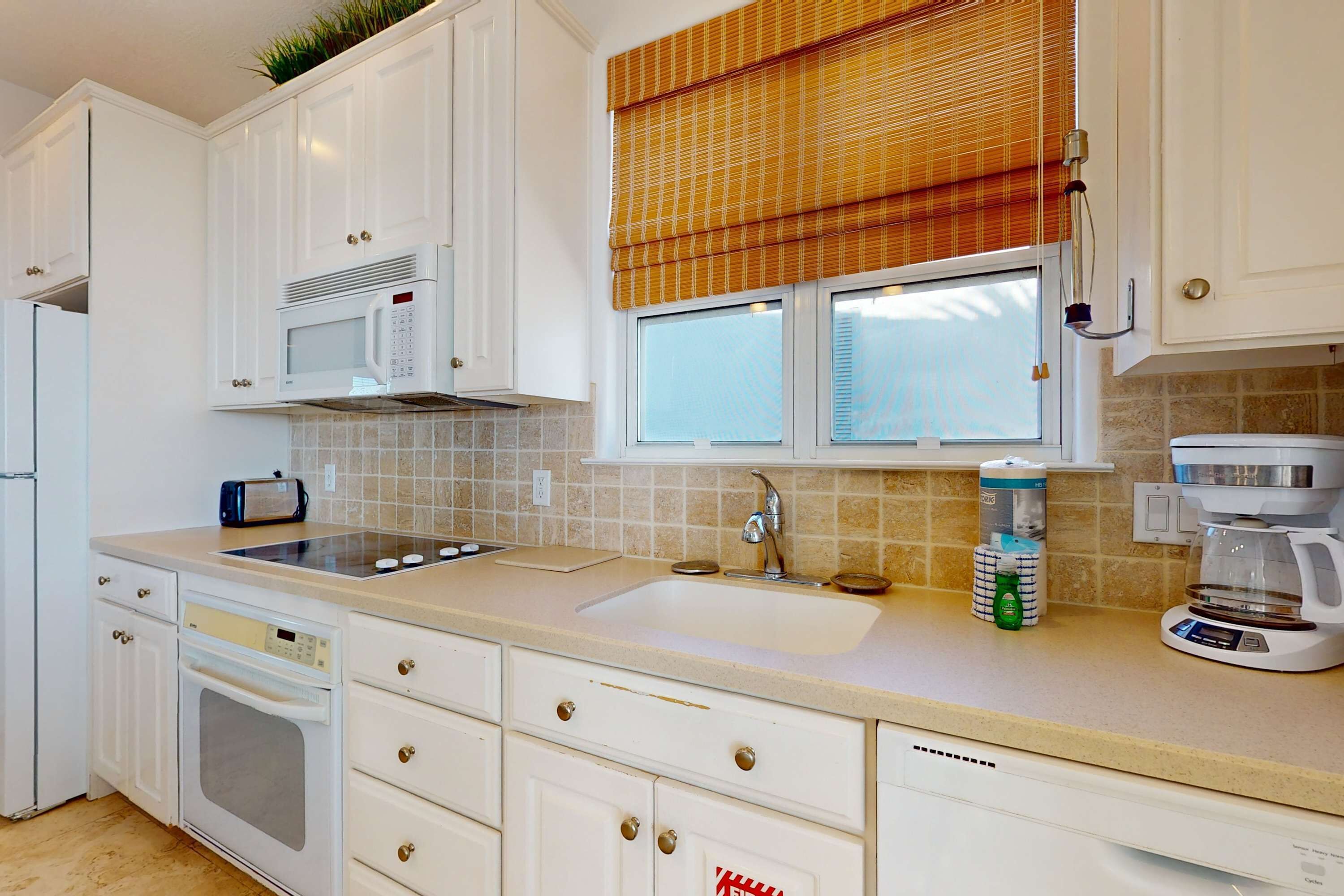 A modern kitchen with white cabinets, a built-in microwave, a coffee maker, and a dishwasher.