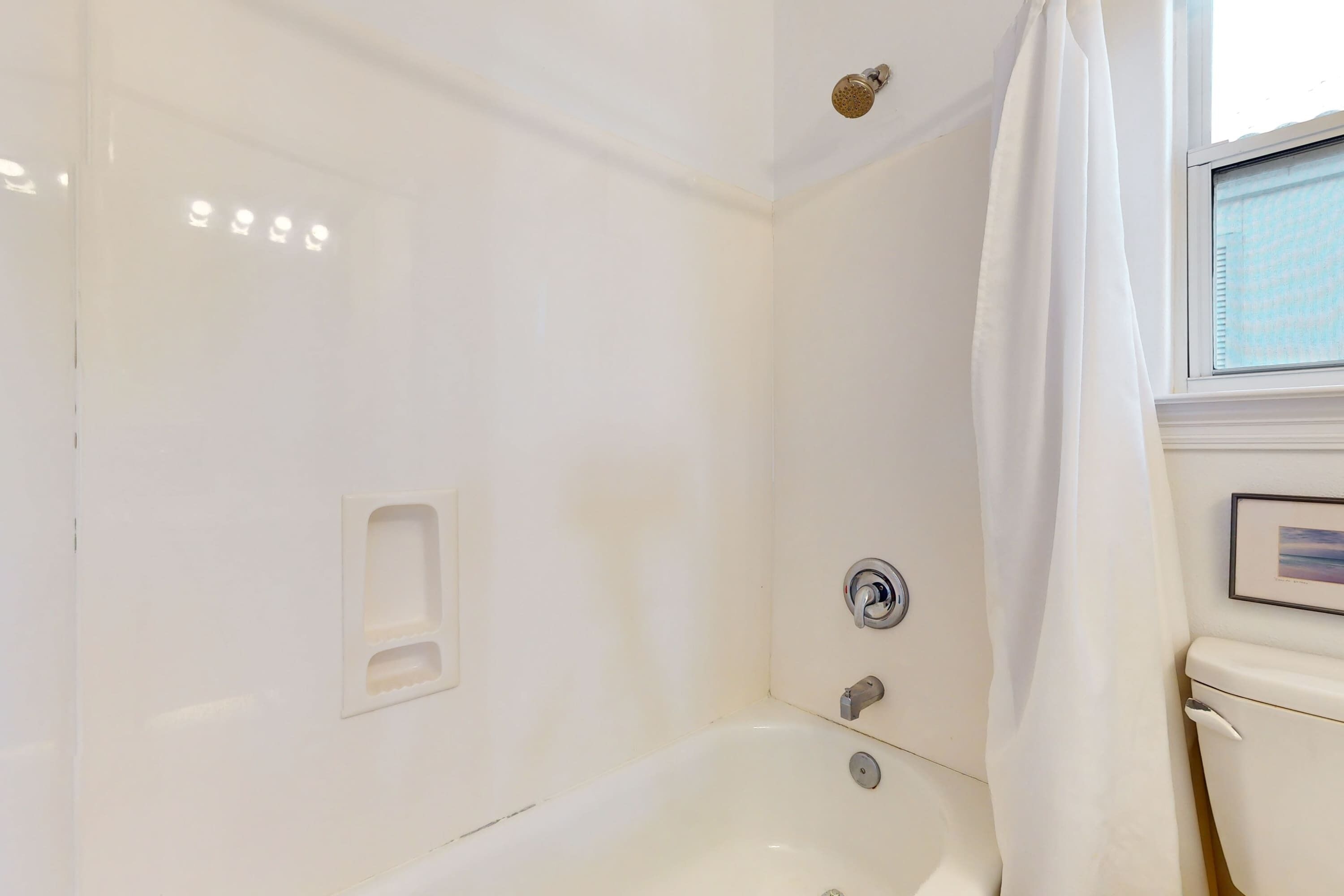 Un baño blanco con bañera, cortina de ducha y inodoro.