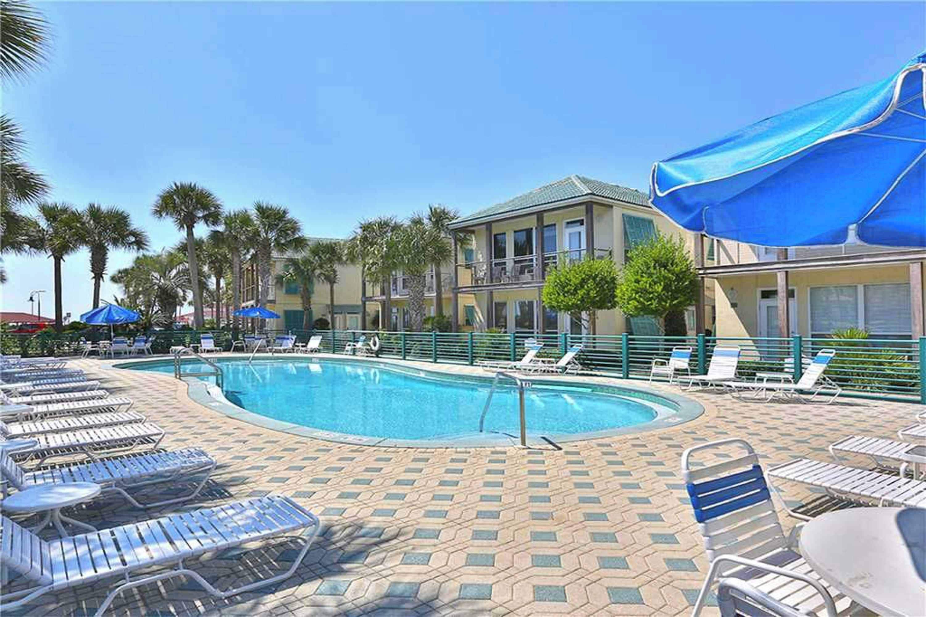 A pool area with lounge chairs and umbrellas, surrounded by palm trees and buildings.
