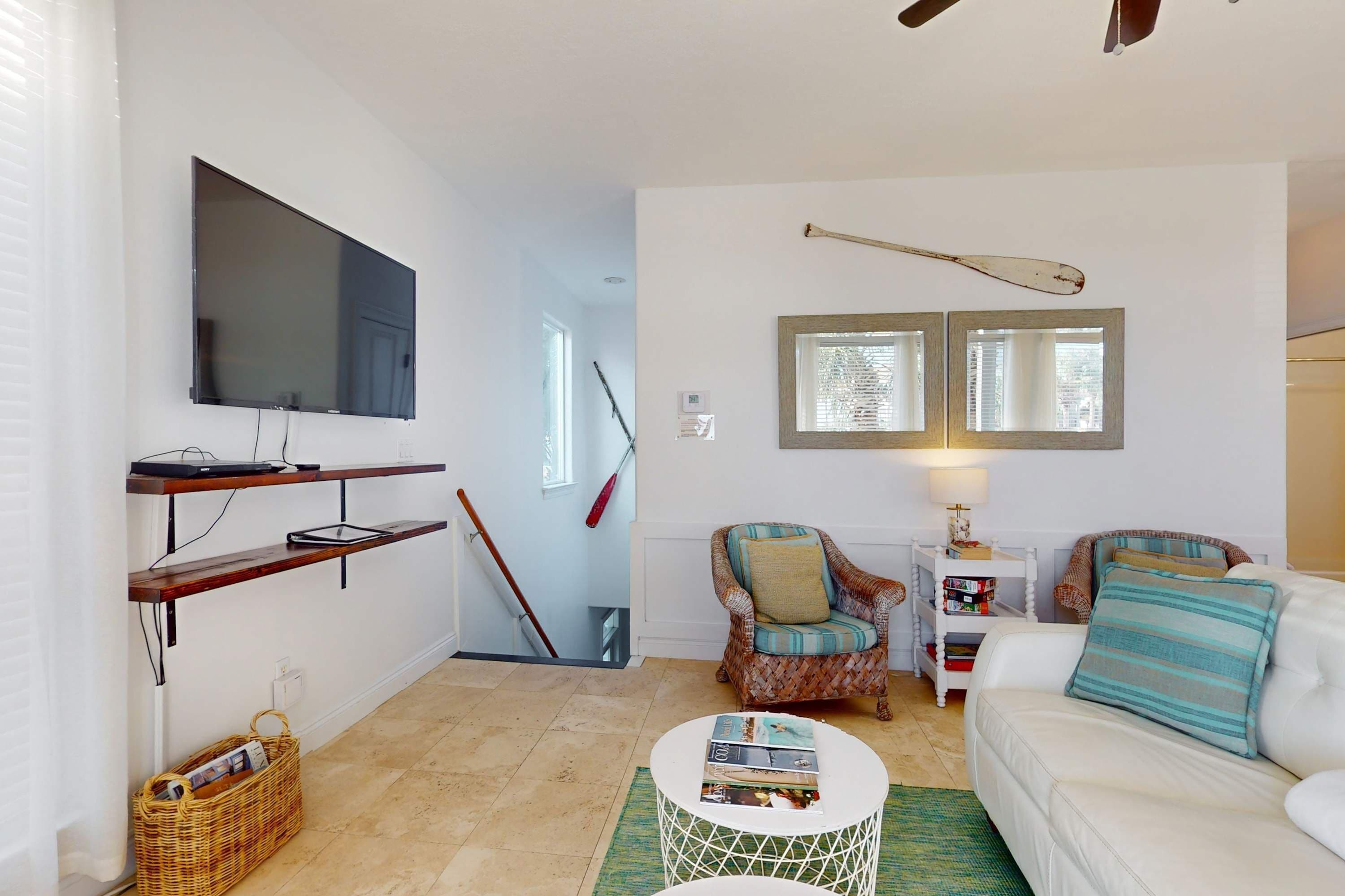Een woonkamer met een flatscreen televisie, een rieten mand, een witte bank en twee fauteuils.