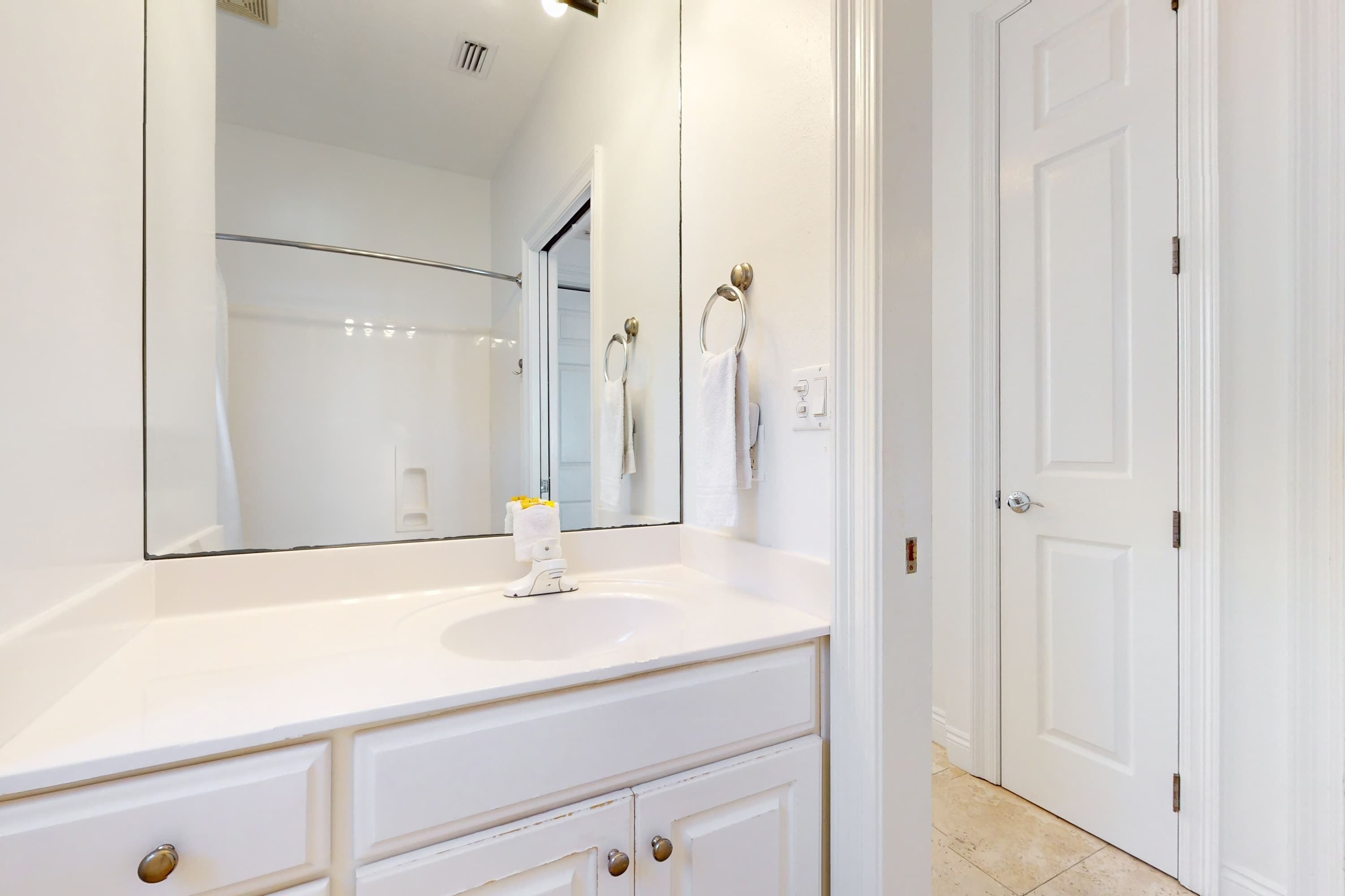 A bathroom with a white vanity, a large mirror, and a door.