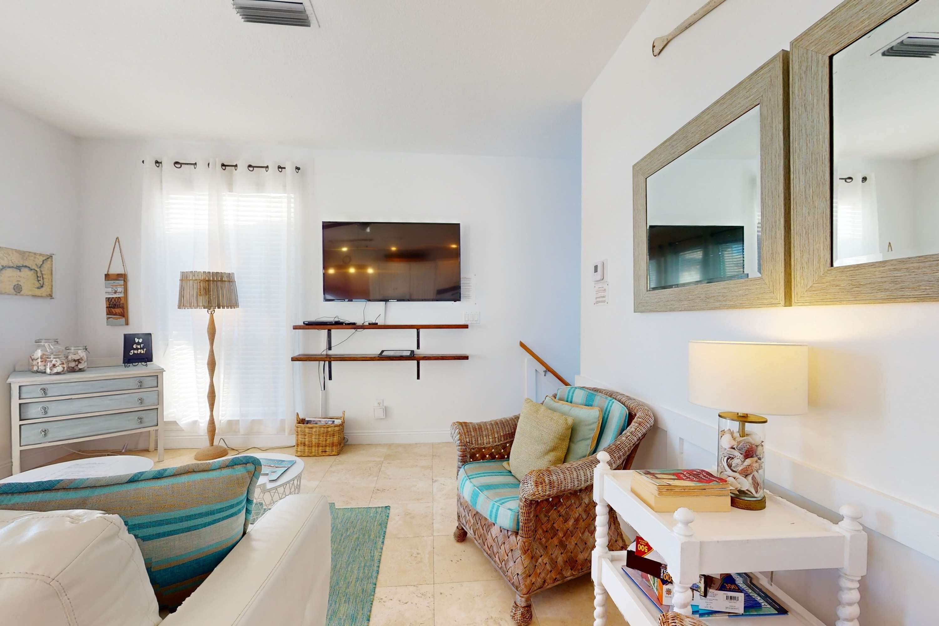 A living room with a sofa, a wicker chair, a TV, a lamp, and a small table with books.