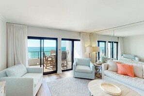 A spacious living room with a large window overlooking the sea, a sofa, a chair, and a coffee table. - Charming oceanfront condo with pool, tennis, balcony & washer&dryer (Destin)