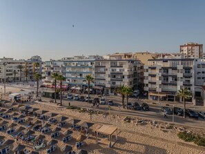Eine Küstenstadt mit mehrstöckigen Gebäuden, einem Sandstrand und Liegestühlen, bewölkter Himmel.