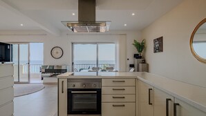 A modern kitchen with a built-in oven, a large window overlooking the sea, and a dining area with a view. - T2 Sunrise Dream-frente MAR (Loulé)