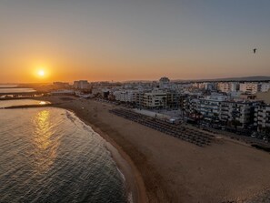 Eine Küstenstadtlandschaft mit Strand, Gebäuden und einem Sonnenuntergang.